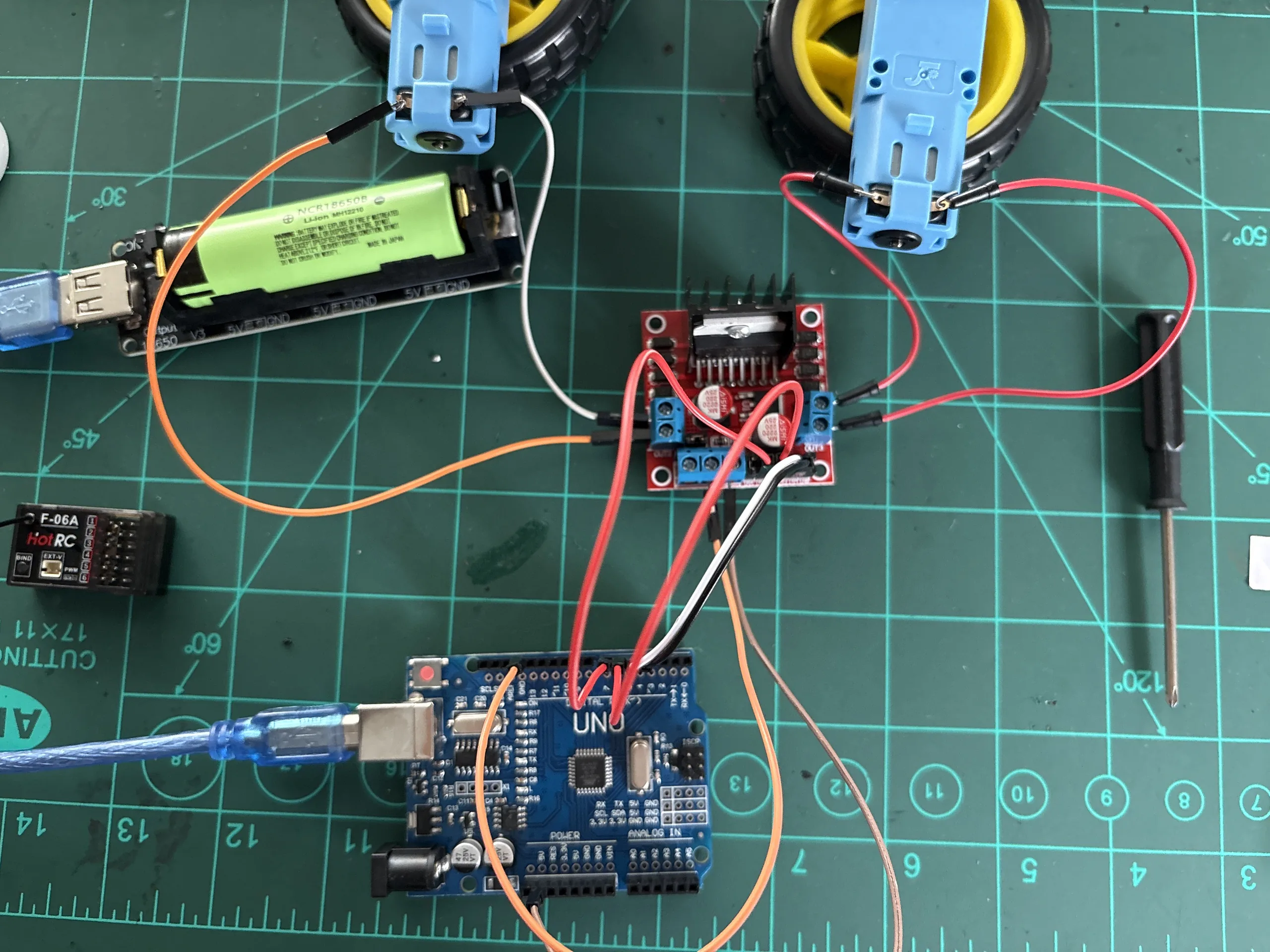 Arduino Uno, motor-driver board, battery module, radio receiver, and two geared motors on a workbench